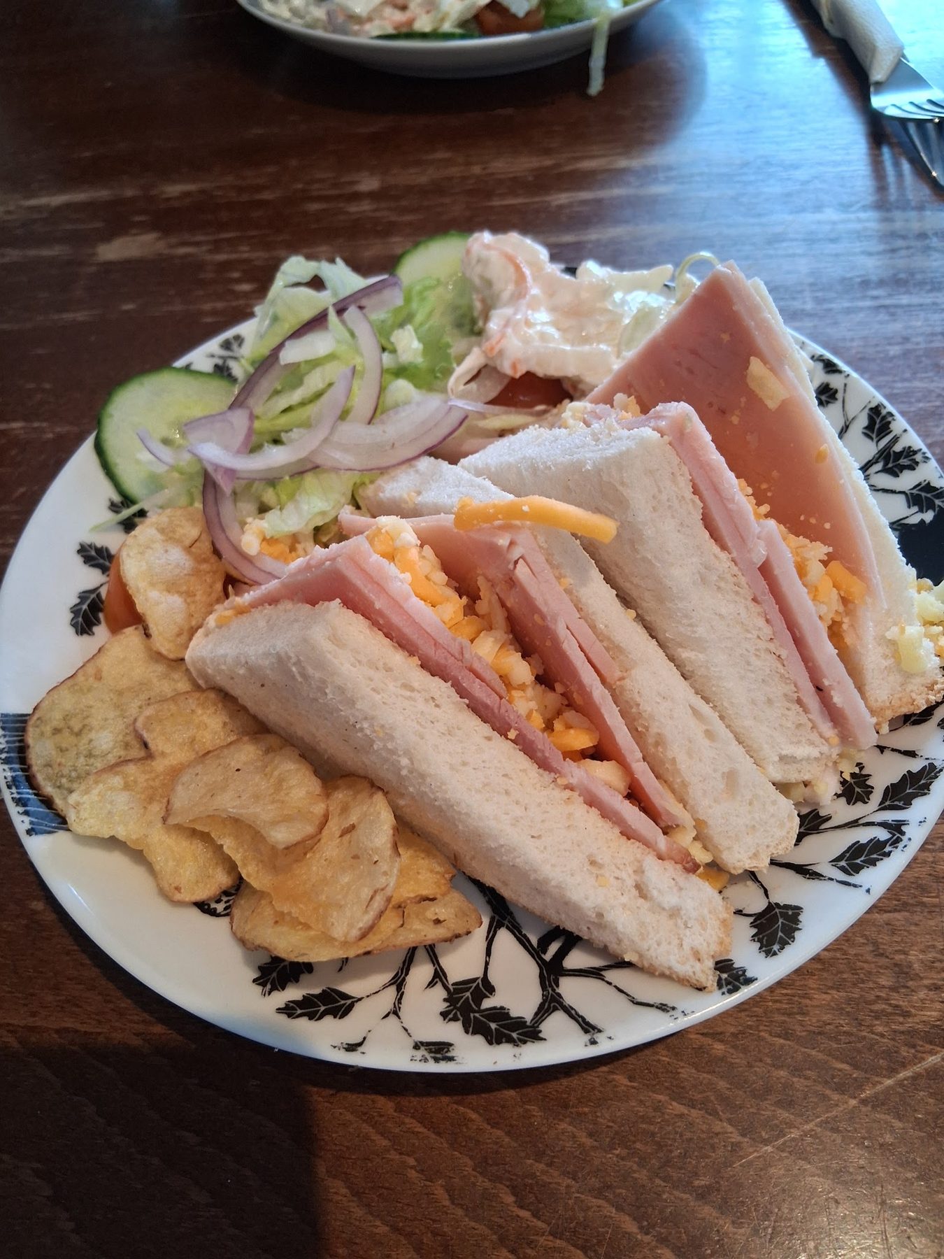 Club sandwiches with crisps, salad and coleslaw on a patterned plate