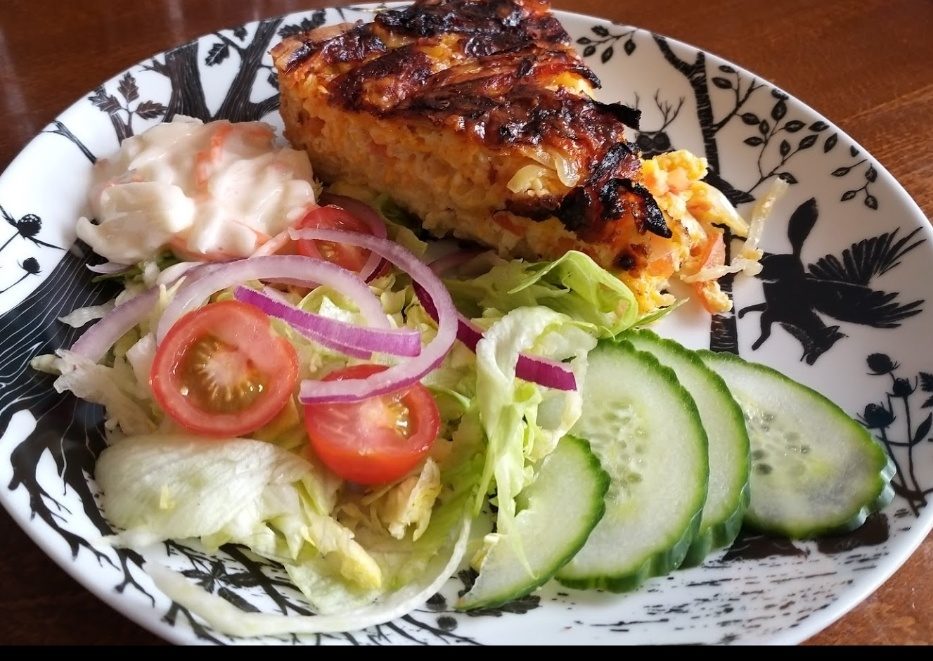 A slice of quiche with salad, tomato, cucumber and coleslaw
